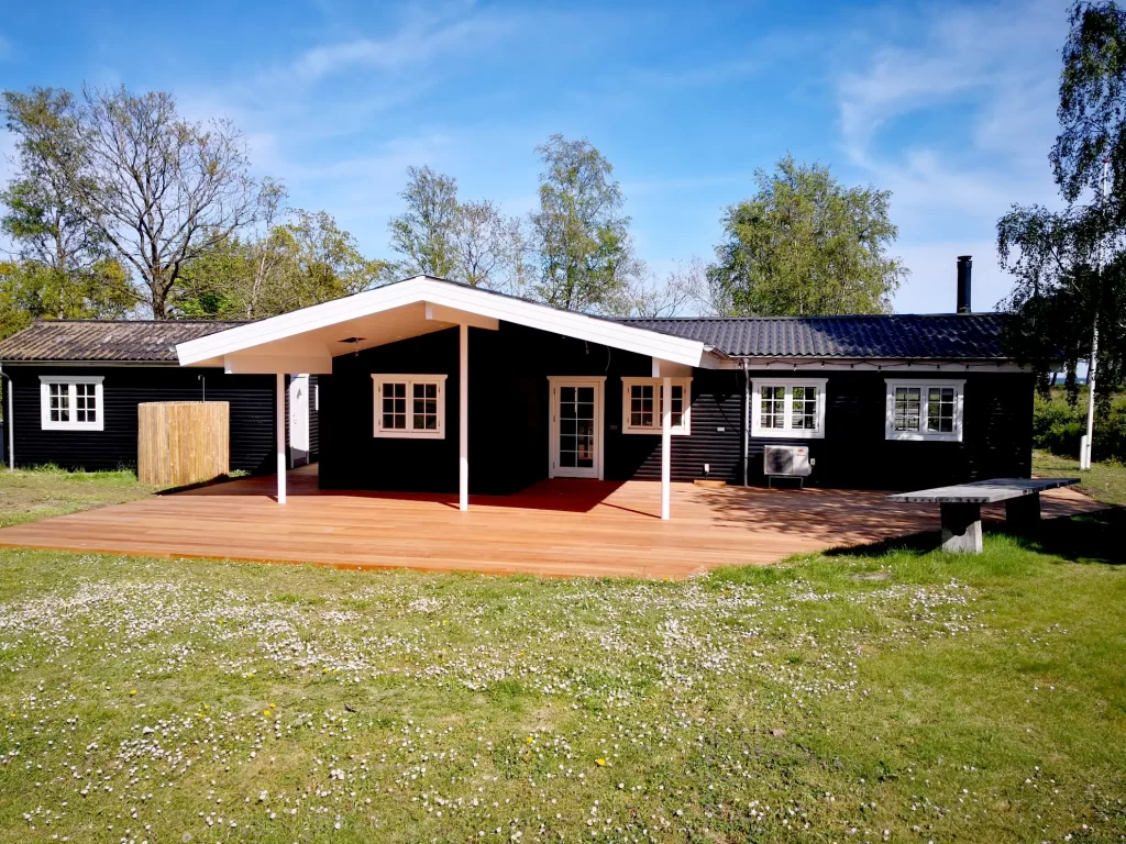 Terrasse i hårdttræ og hårdttræ strøer. Træsort er guariuba. Terrasse startede med at være meget gul, i løbet af få uger blev den mere brun, efter flere uger var den meget brun og efter et halvt år blev den sølvgrå. Sommerhuset er beliggende i Saksild